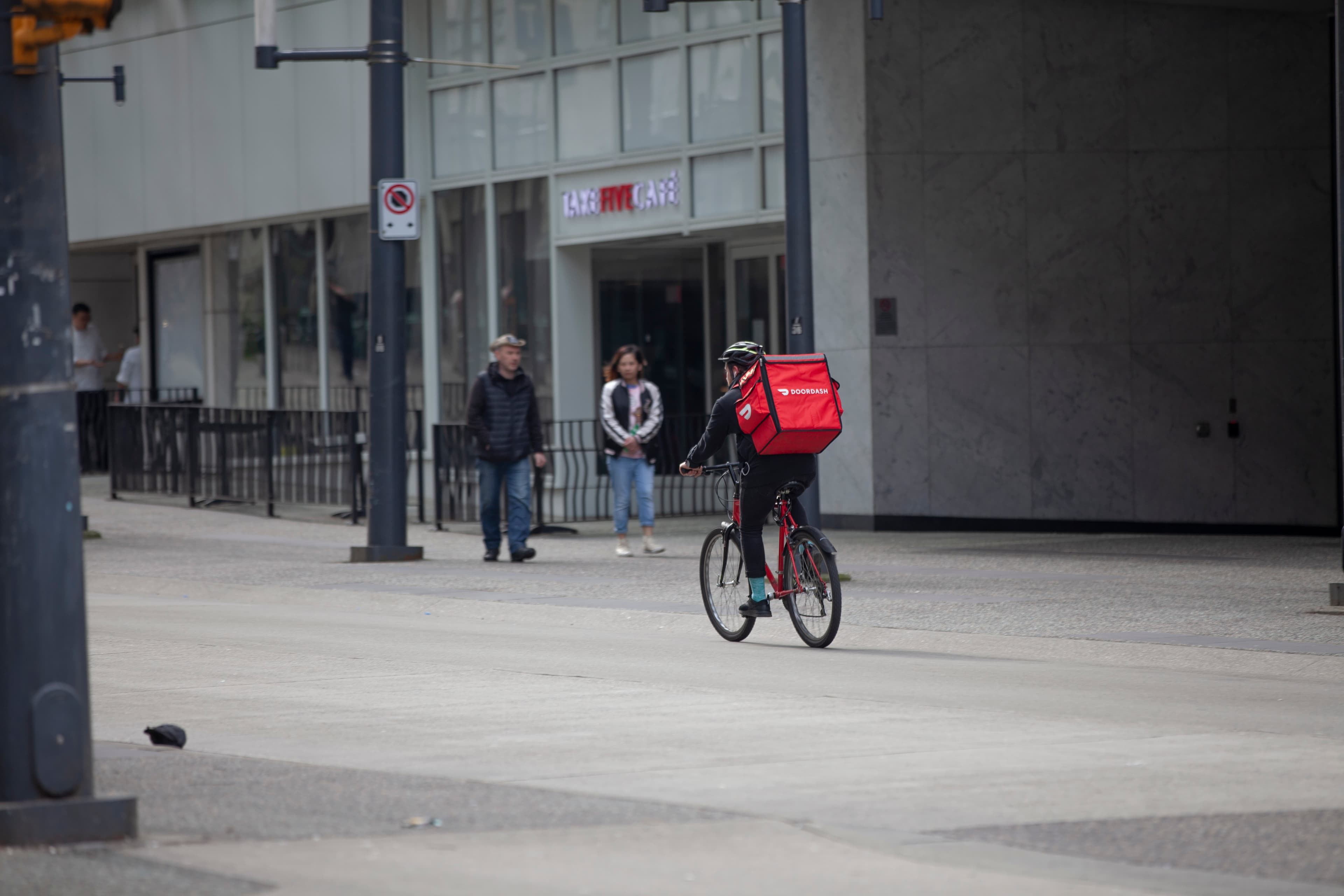Un repartidor en bicicleta lleva una mochila roja de DoorDash en Granville Street, en el centro de Vancouver.