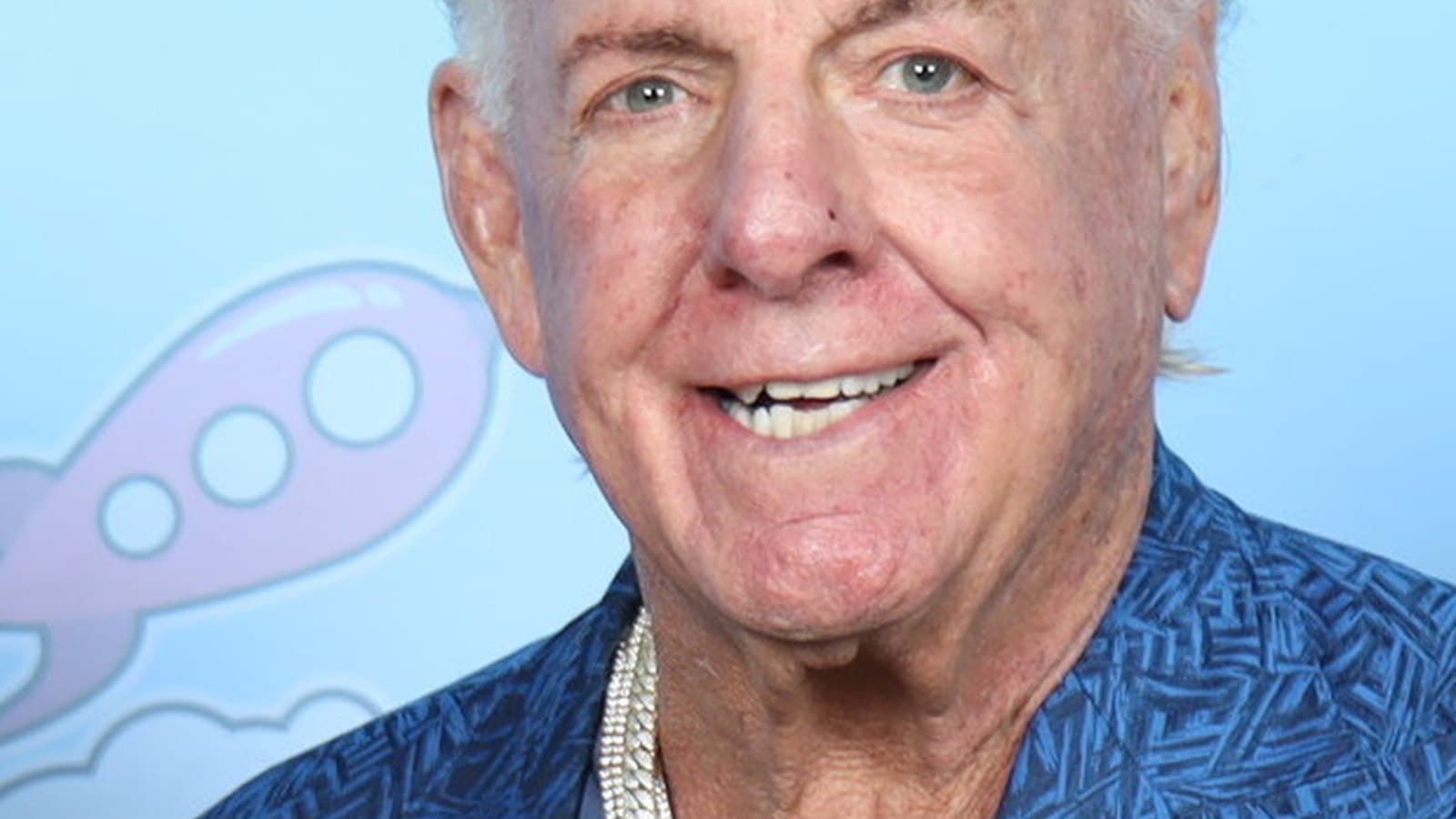 Ric Flair smiling at a fan convention photo op in 2023.