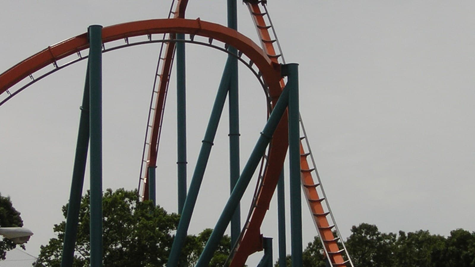 Orange track and green supports of the Goliath roller coaster against a gray sky.