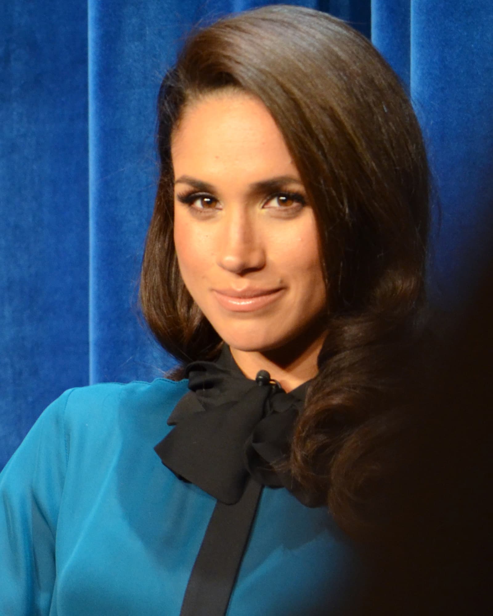 Meghan Markle at a Suits panel at the Paley Center in January 2013, in a solo portrait against blue curtains.