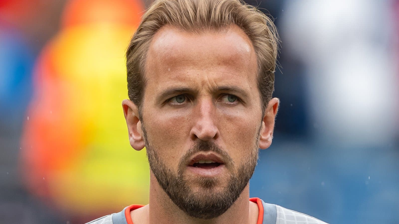 Close-up of Harry Kane, with short swept-back hair and a beard, wearing a gray England shirt with an orange collar at England's World Cup match against Ghana in June 2026.