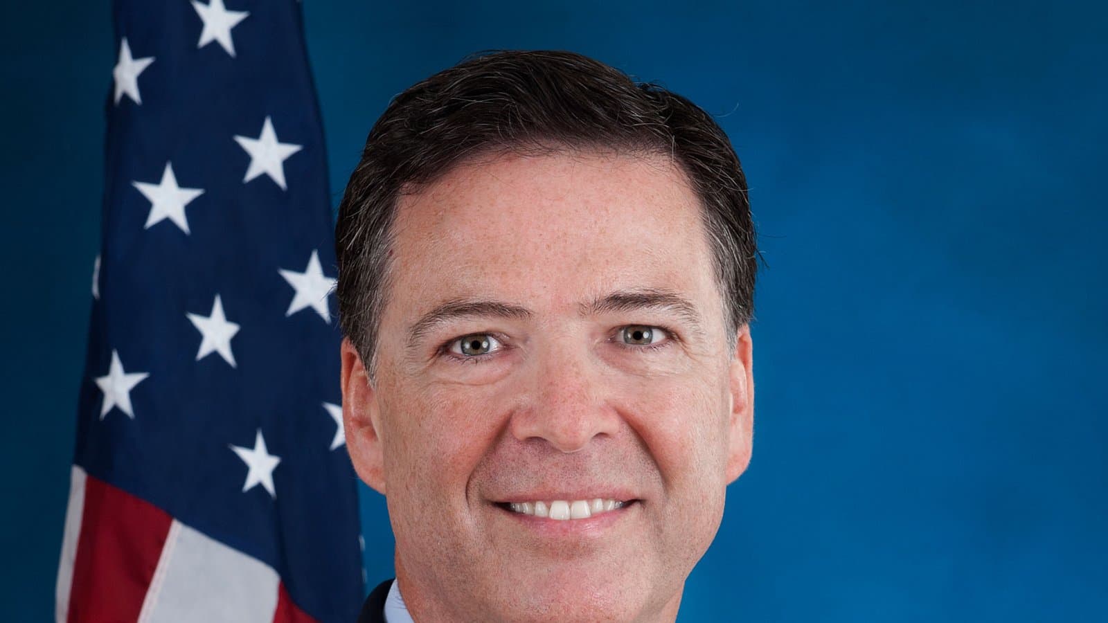 Retrato oficial de James Comey como director del FBI: un hombre sonriente de cabello oscuro y corto, con traje oscuro, camisa celeste y corbata roja, frente a un fondo azul y una bandera de EE. UU.