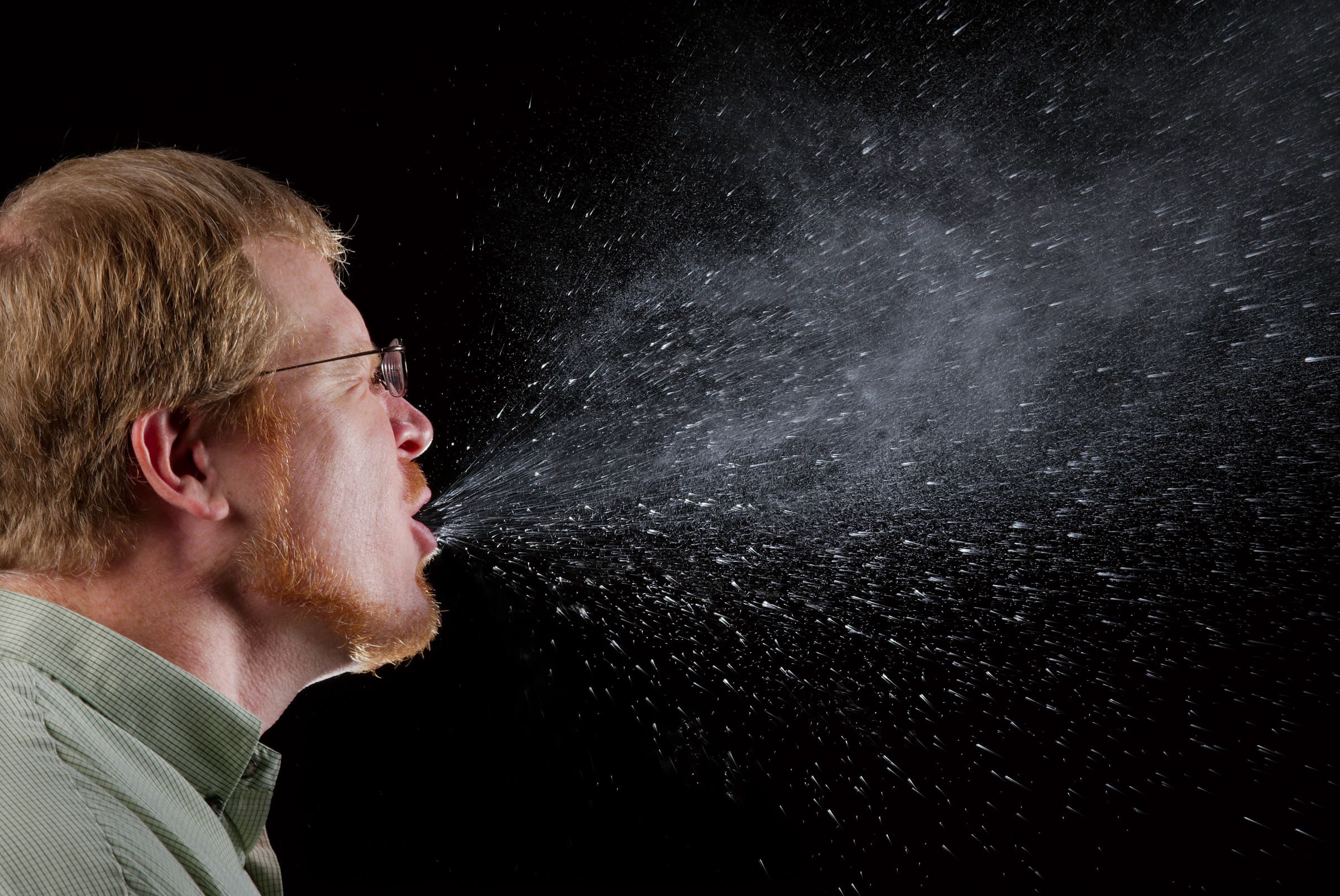 Archival 2009 photograph of a man sneezing, with visible droplets against a dark background.